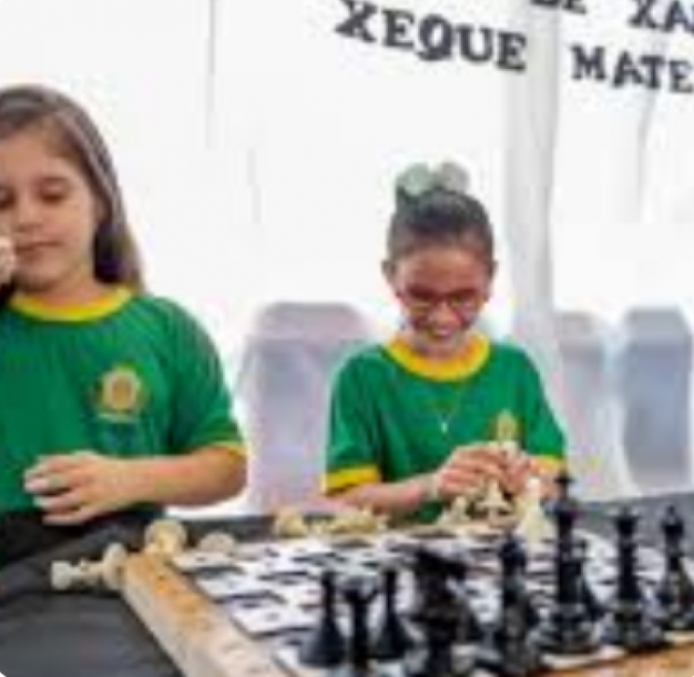 Crianças com roupa verde com um tabuleiro de xadrez sob a mesa